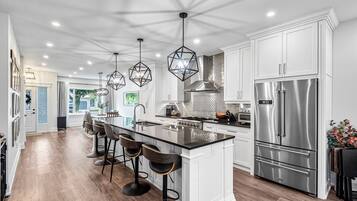 A modern kitchen with a central island, bar stools, stainless steel appliances, and pendant lighting.