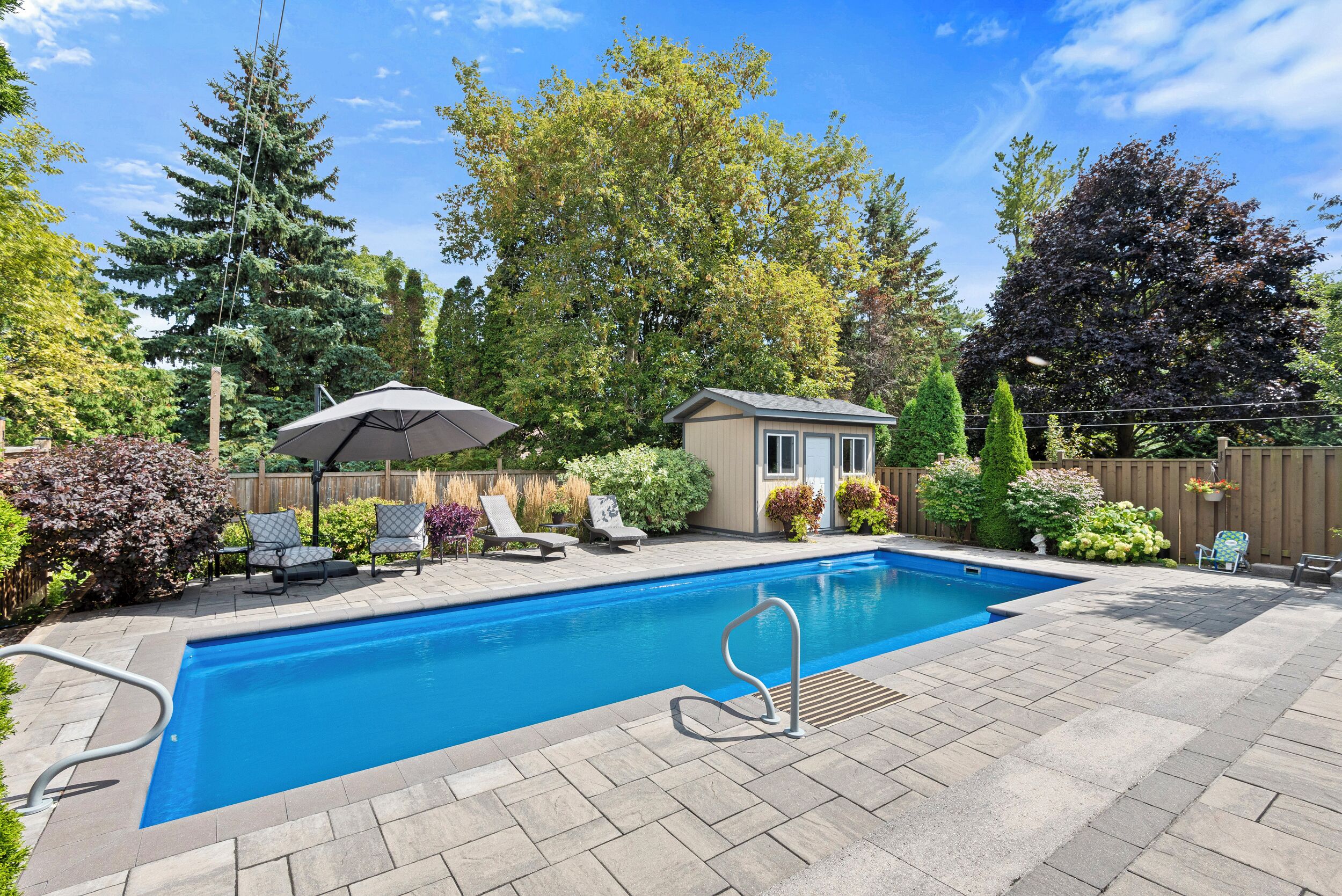 A rectangular swimming pool with a diving board, surrounded by a patio with lounge chairs and a small shed.