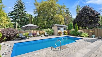 A rectangular swimming pool with a diving board, surrounded by a patio with lounge chairs and a small shed.