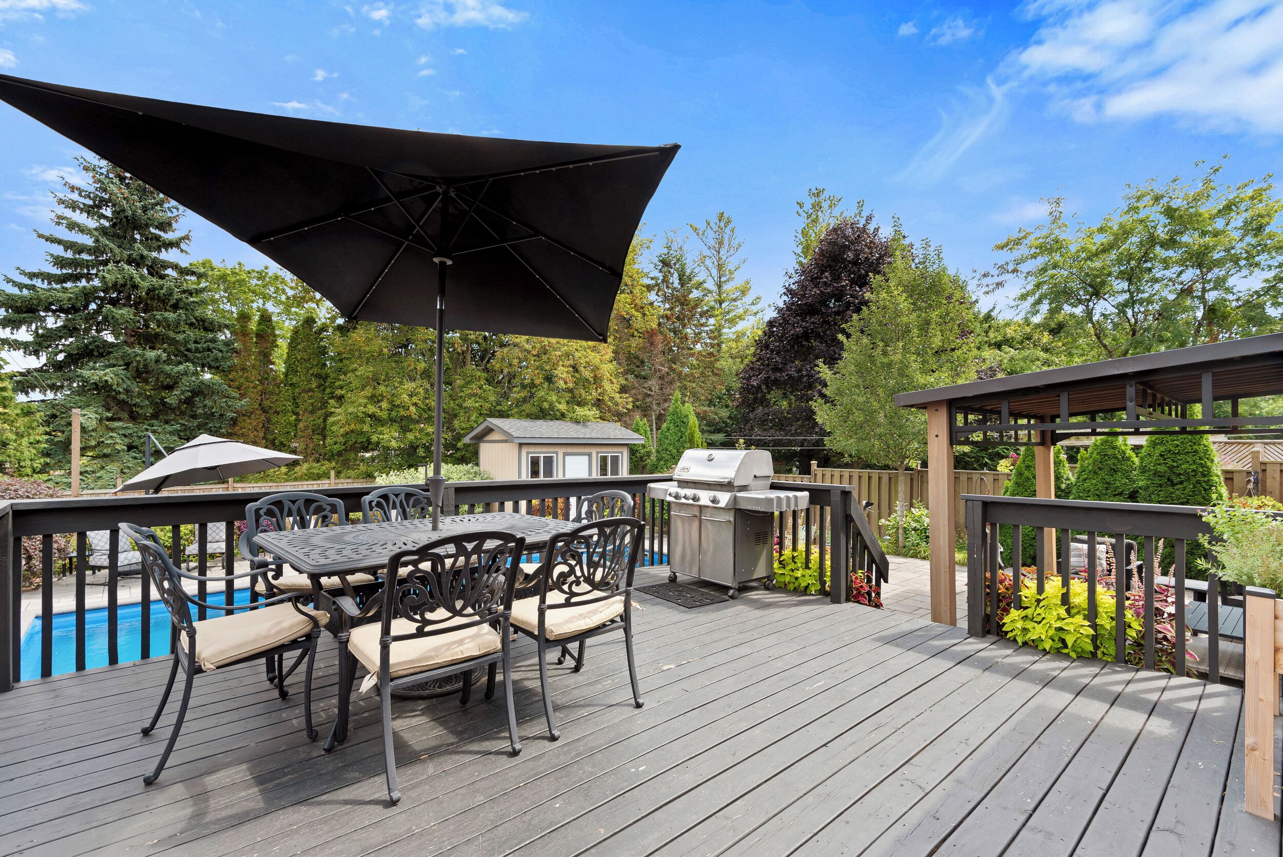 A deck with a table and chairs, a grill, and a pool.