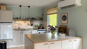Una cocina con armarios blancos, una isla central, un lavamanos, una estufa y una ventana con persianas.