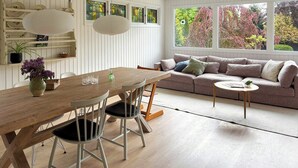 Una habitación con una mesa de madera para comer, sillas, un sofá y una ventana con follaje otoñal.