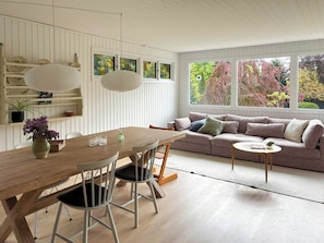Una habitación con una mesa de madera para comer, sillas, un sofá y una ventana con follaje otoñal.