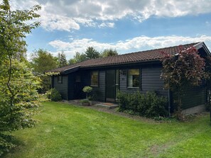 A small, dark-colored house with a tiled roof, surrounded by a well-maintained lawn and various shrubs. - Classic wooden house with private garden near sea (Gilleleje)