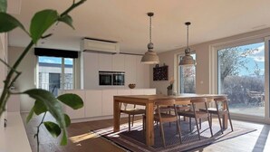 Eine moderne Küche mit integrierten Geräten, ein Essbereich mit Holztisch und -stühlen sowie große Fenster mit Blick ins Freie.