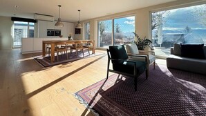 Ein moderner Wohnraum mit Küche, Essbereich und großen Fenstern mit Blick ins Freie.
