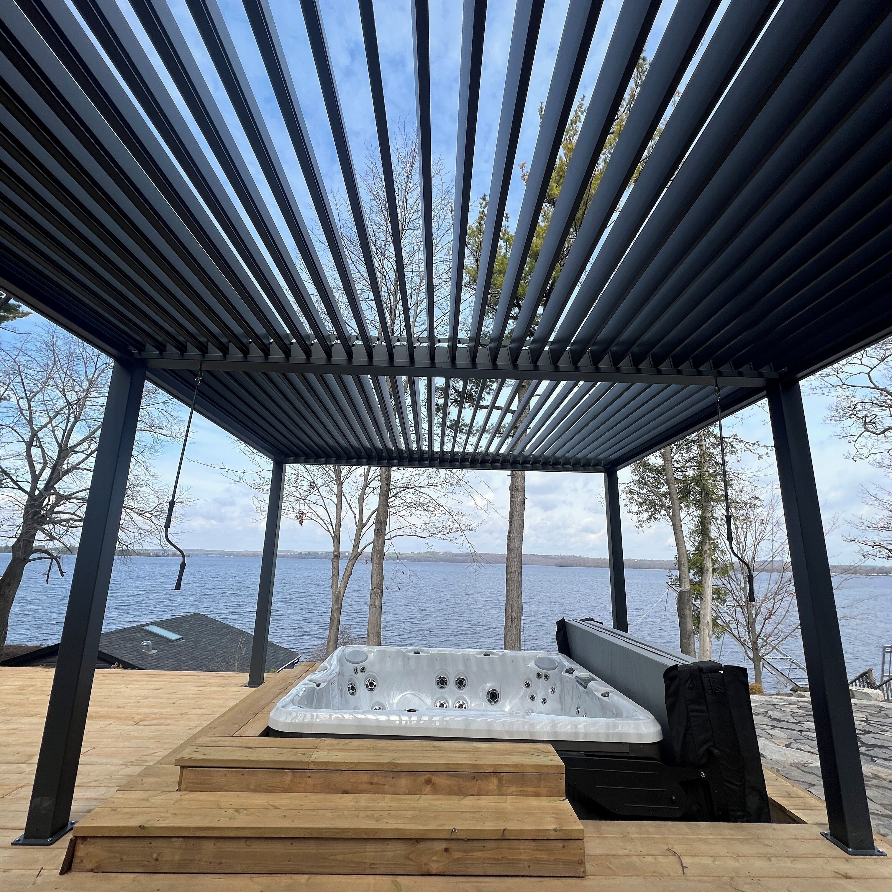 A wooden deck with a hot tub, a pergola overhead, and a view of the water.