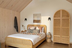 A room with a wooden bed, a rattan wardrobe, and a wall-mounted artwork.