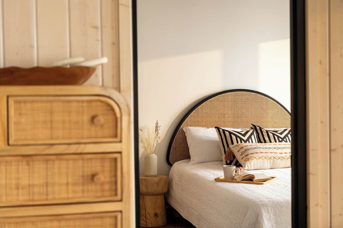 A bedroom with a bed, a wooden dresser, a small side table, and a woven headboard.