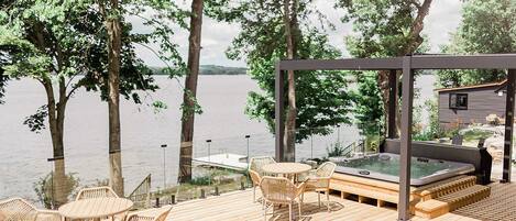 A wooden deck with outdoor furniture, a hot tub, and a view of a lake.