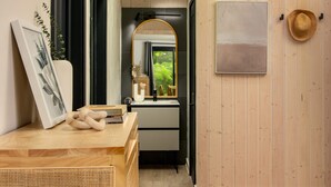 A narrow hallway with wooden walls, a ceiling light, a framed picture, a hat, and a mirror reflecting greenery. - Away Cabins (Roseneath)