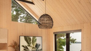 A modern interior with a wooden ceiling, a large window with a view of trees, a television, and a fireplace. - Away Cabins (Roseneath)