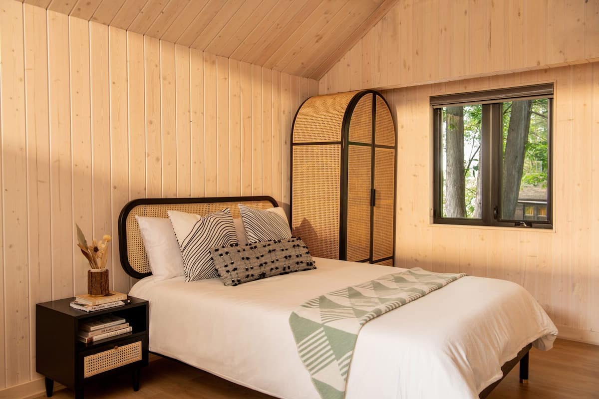 A wooden-paneled bedroom with a bed, a nightstand, a window, and a woven partition.