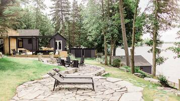 A lakeside cabin with outdoor seating, a fire pit, and a stone patio.