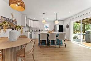 A modern kitchen with white cabinets, a central island with bar stools, and a dining area with a round table and chairs.