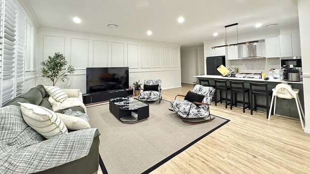 A modern living room with a flat-screen TV, sofas, a coffee table, and a kitchen area with a bar and counter.