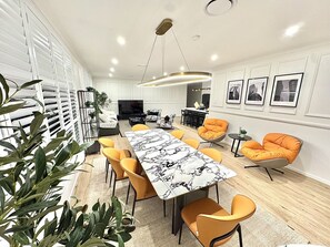 A modern dining area with a marble table, orange chairs, and a pendant light. - Spacious Luxury Home of 8 bedroom in Menangle Park (Menangle Park)
