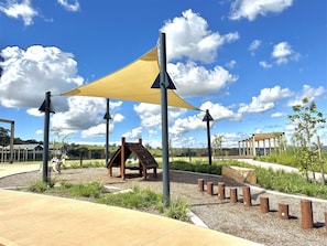 A playground with climbing structures, a shaded area, and a wooden playhouse.