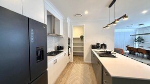 A modern kitchen with a refrigerator, stove, and microwave. There is a dining area with a table and chairs. - Spacious Luxury Home of 8 bedroom in Menangle Park (Menangle Park)
