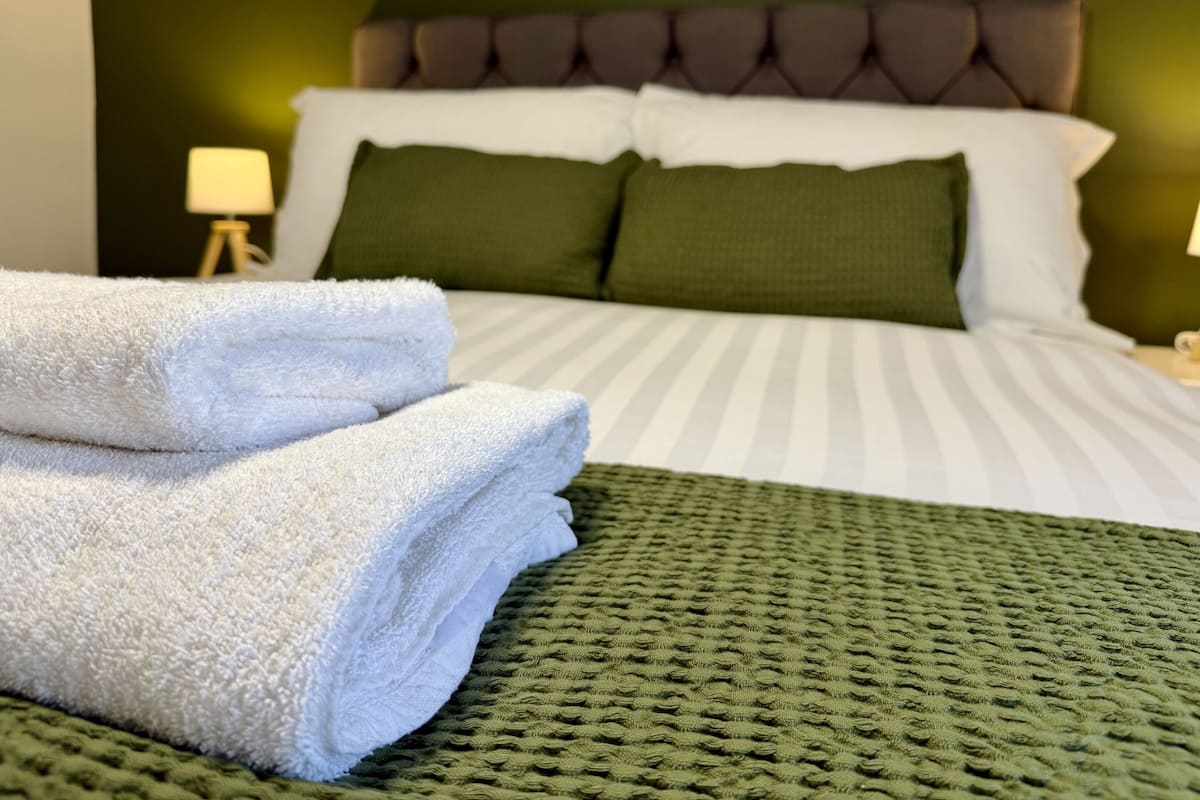 A neatly made bed with white and green bedding, a green throw blanket, and two folded white towels.