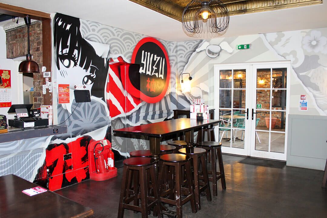 Interior de restaurante con mostrador, taburetes y un mural.