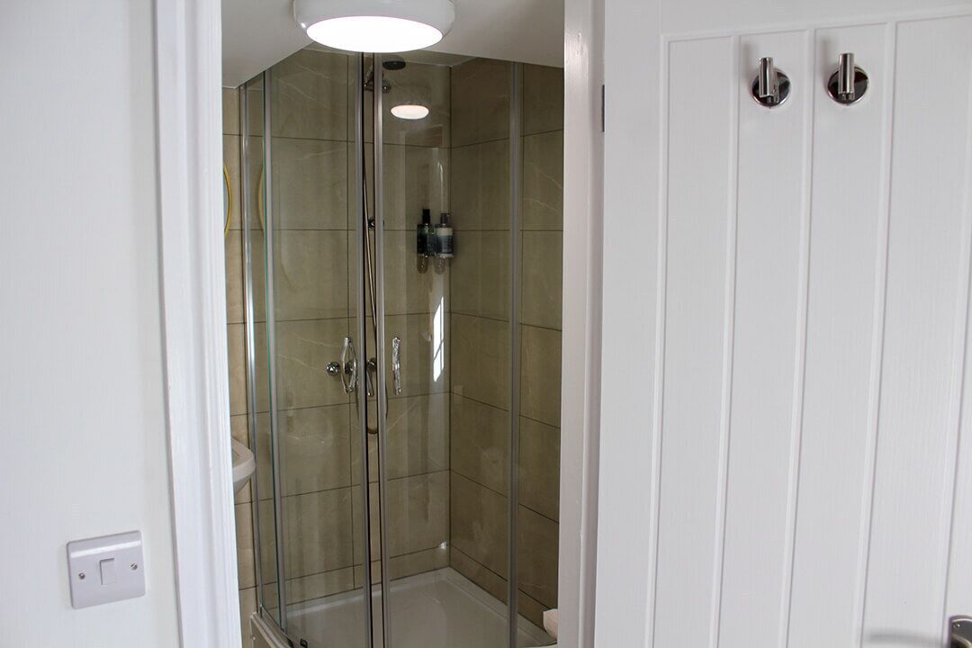 Une cabine de douche fermée par des parois en verre, avec une porte blanche et un luminaire au-dessus.