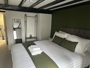 Una cama bien tendida con sábanas blancas y detalles en verde, una mesita de noche con una botella y una escalera fijada a la pared.