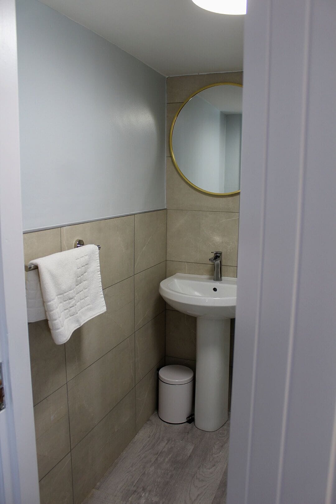 Un baño con un lavabo blanco, un espejo redondo con marco dorado y una toalla blanca en un perchero.