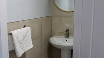 Un baño con un lavabo blanco, un espejo redondo con marco dorado y una toalla blanca en un perchero.