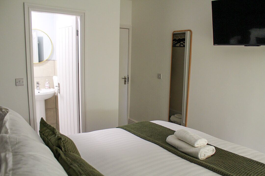 Habitación de hotel con cama, espejo, televisor y baño visible a través de una puerta abierta.