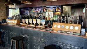 Um bar com balcão de madeira, diversas torneiras de cerveja e banquetas.