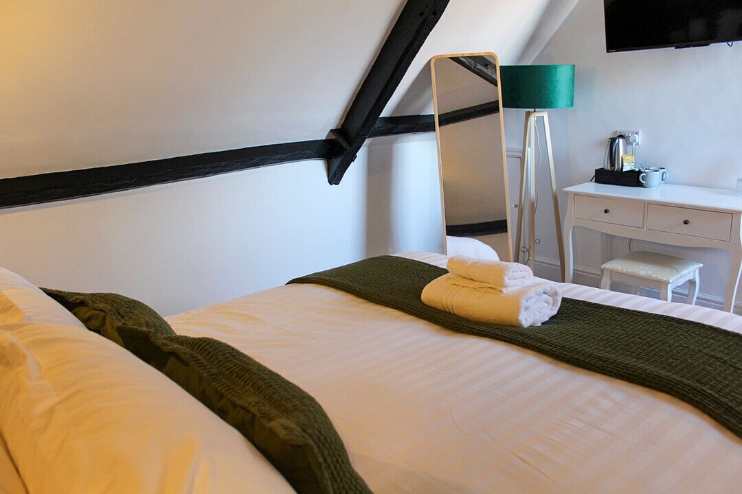 A hotel room with a bed, a desk, a chair, a mirror, and a television.