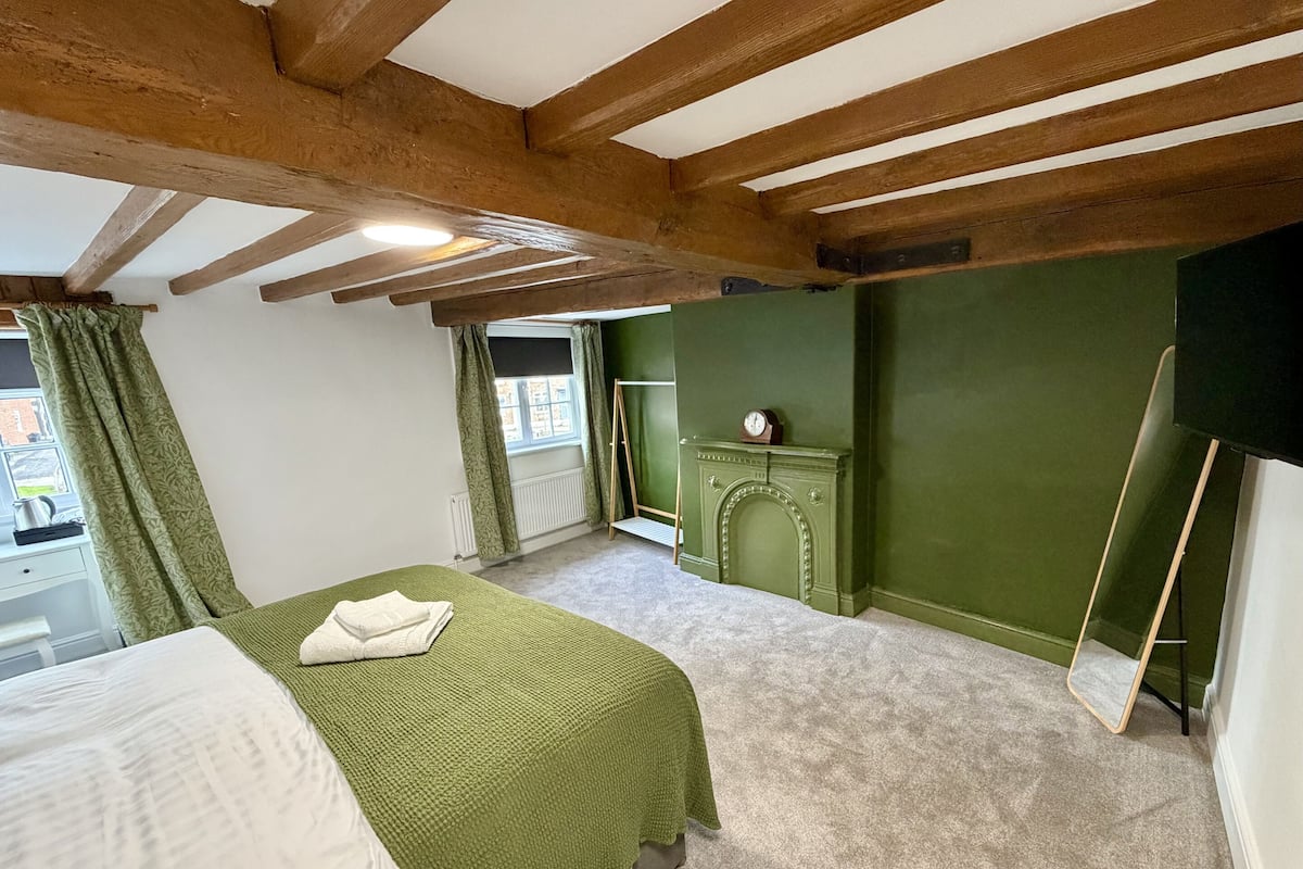 A bedroom with a bed, a green wall, a fireplace, and a window.