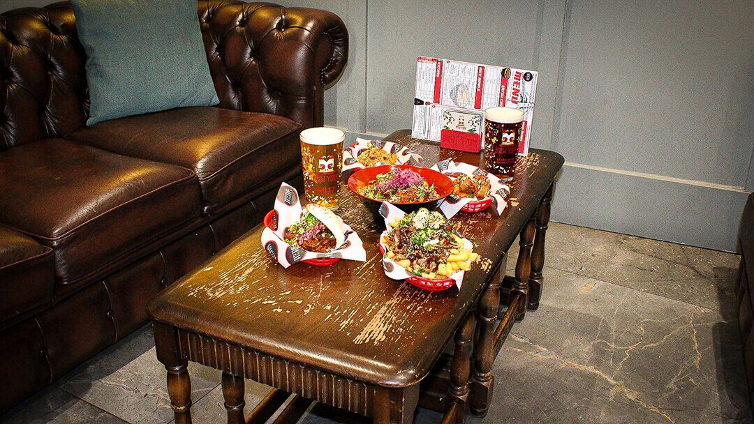 A dining table with food and drinks, a leather couch, and a menu stand.