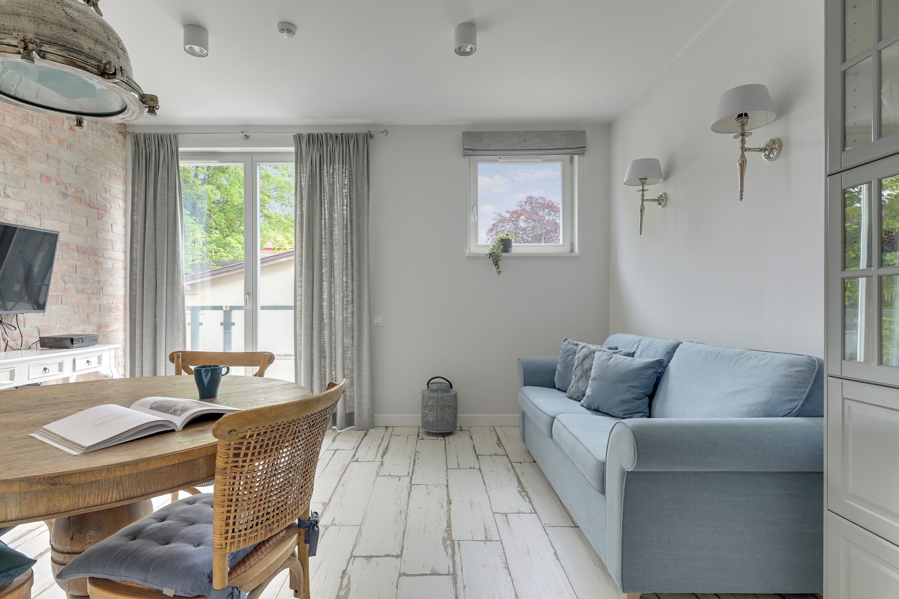 A living room with a wooden table, a blue sofa, a television, and a window with curtains.