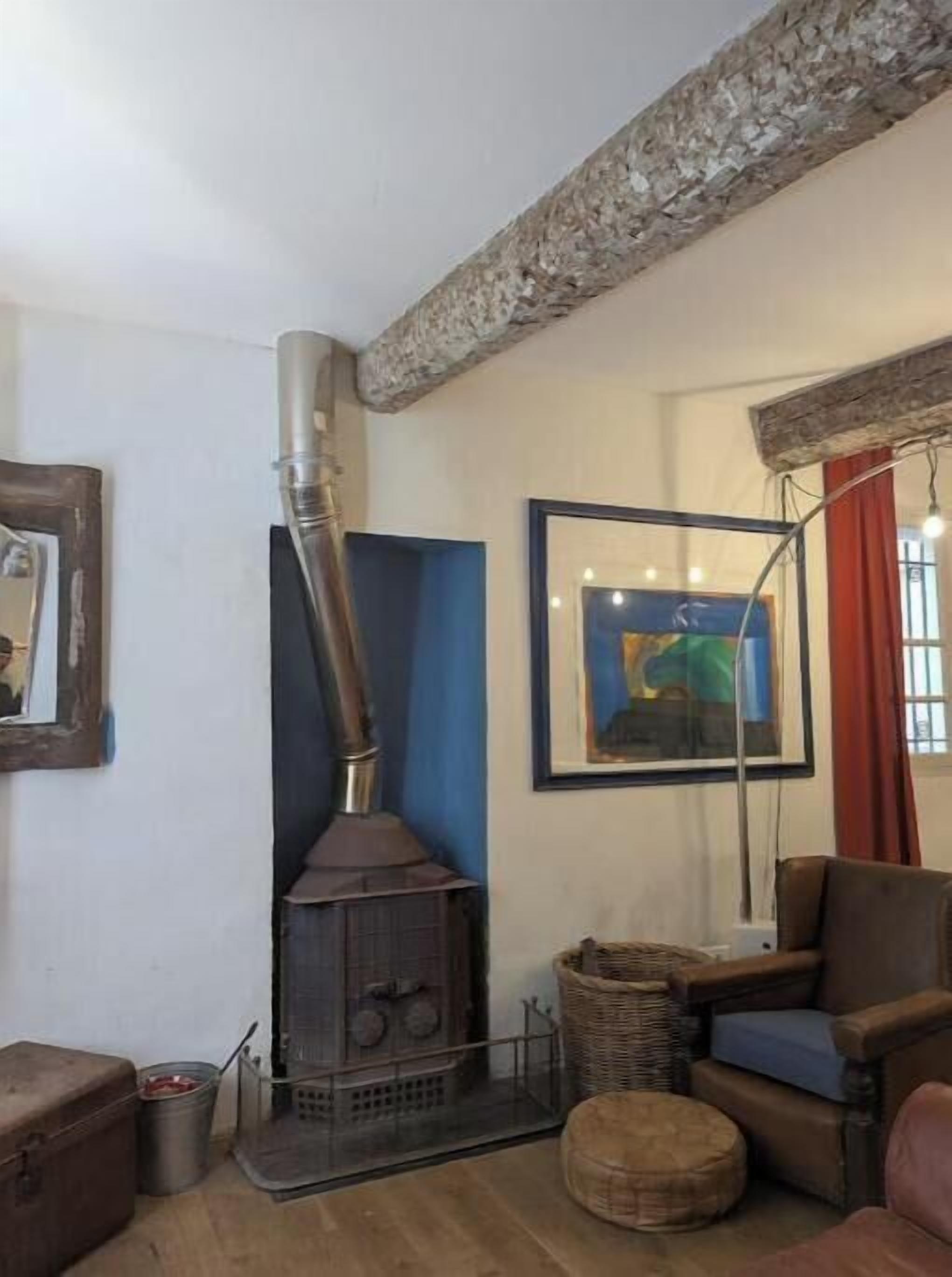 A room with a wood stove, a framed painting, a wicker basket, a leather chair, and a metal bucket.