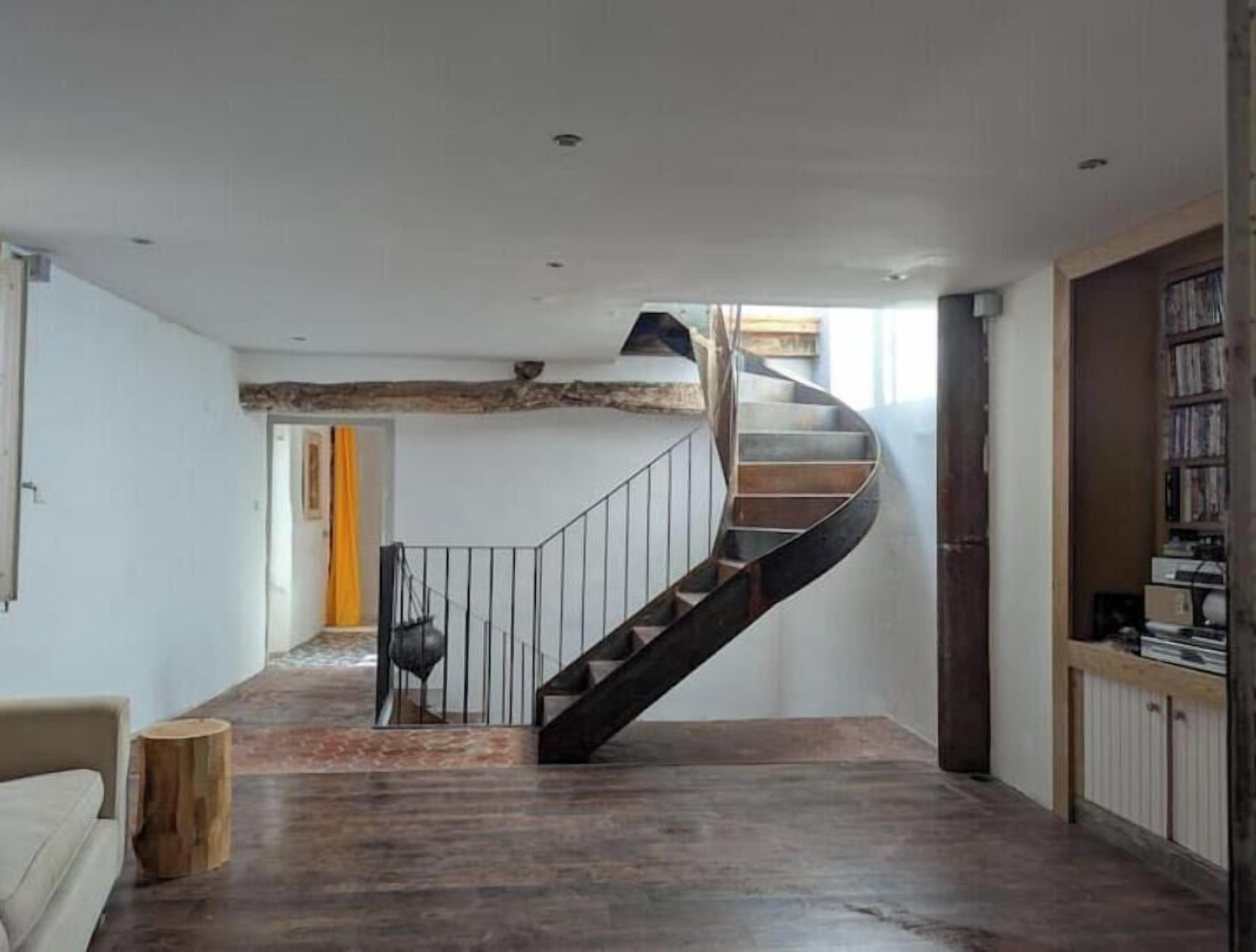 A spacious room with a curved staircase, a wooden floor, and a bookshelf.