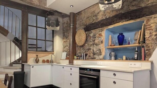 Una cocina moderna con gabinetes blancos, horno empotrado y una pared decorativa de piedra.