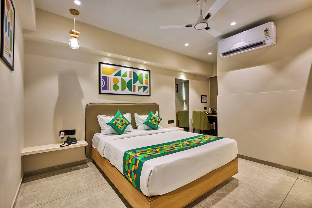 A hotel room with a bed, a bedside phone, a ceiling fan, an air conditioning unit, and a wall-mounted artwork.