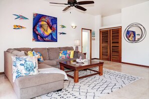 A living room with a sofa, coffee table, and decorative wall art. - Spacious Condo w/ Balcony, Pools + Ocean Views (San Pedro Town)