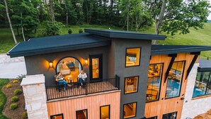 Et moderne hus med flere etager, en balkon, store vinduer og en stenstolpe.