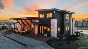 Et moderne hus med en overdækket terrasse, stensøjler og udsigt til solnedgang.