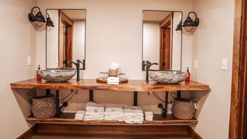 A bathroom with two sinks, each with a large stone basin and a mirror above. There are towels and a soap dispenser on the counter.