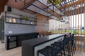 A modern bar area with a counter, black bar stools, and a sign indicating 'Area Gourmet.' - Breeze Residence #410 Beachfront by Carpediem (João Pessoa)
