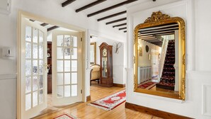 Un pasillo con piso de madera, un espejo grande y ornamentado, y un tapete de diseño rojo y blanco.
