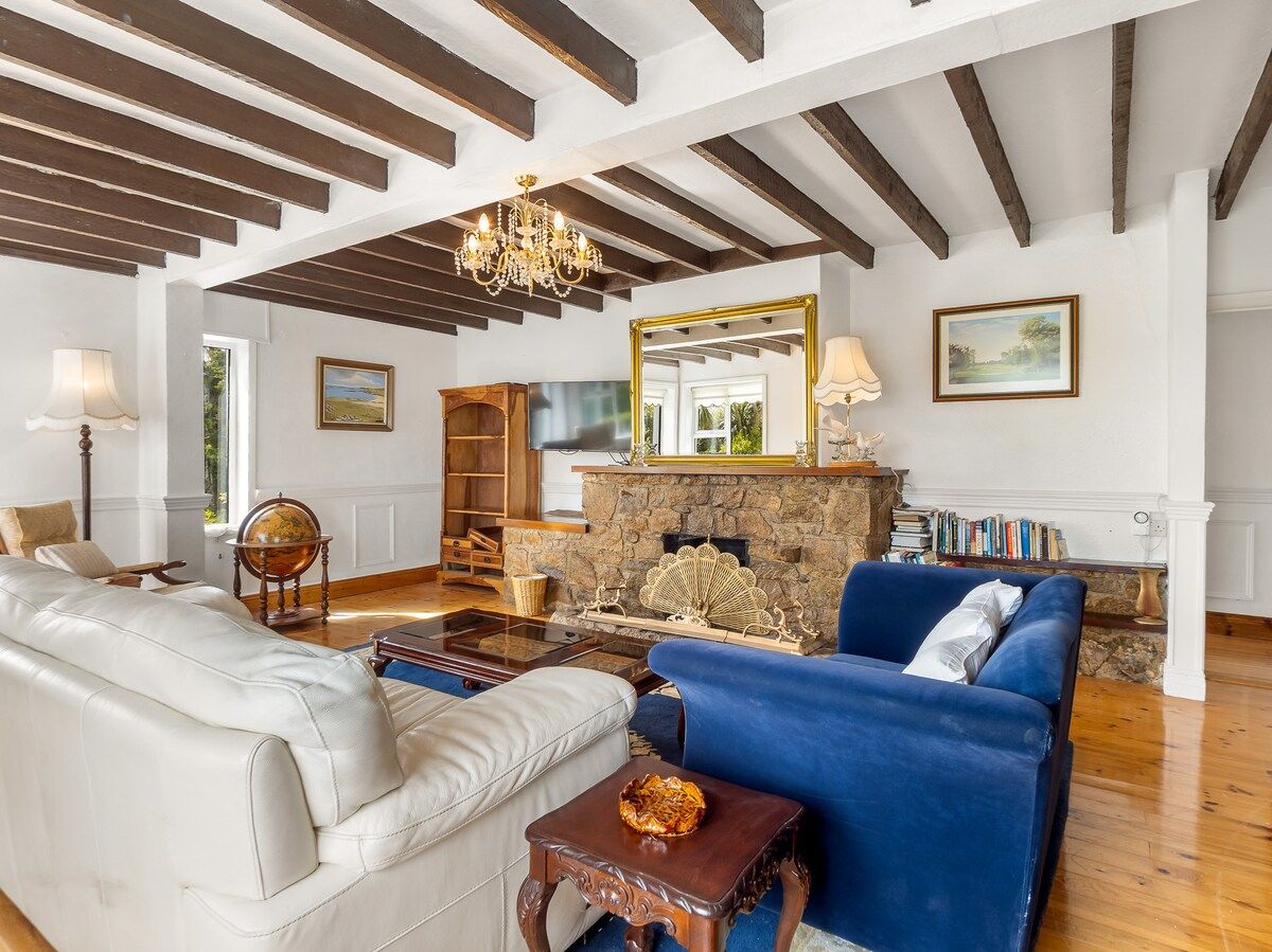 A spacious living room with a stone fireplace, a chandelier, and a large mirror.