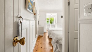 Un pasillo con paredes blancas, piso de madera, un picaporte de latón y un cuadro enmarcado.