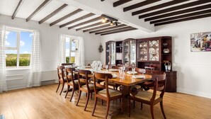 Un comedor con una mesa de madera, sillas, un armario con puertas de vidrio y una ventana con cortinas.