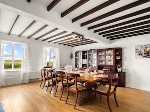 Ein Esszimmer mit einem Holztisch, Stühlen, einer Schranke mit Glastüren und einem Fenster mit Vorhängen.