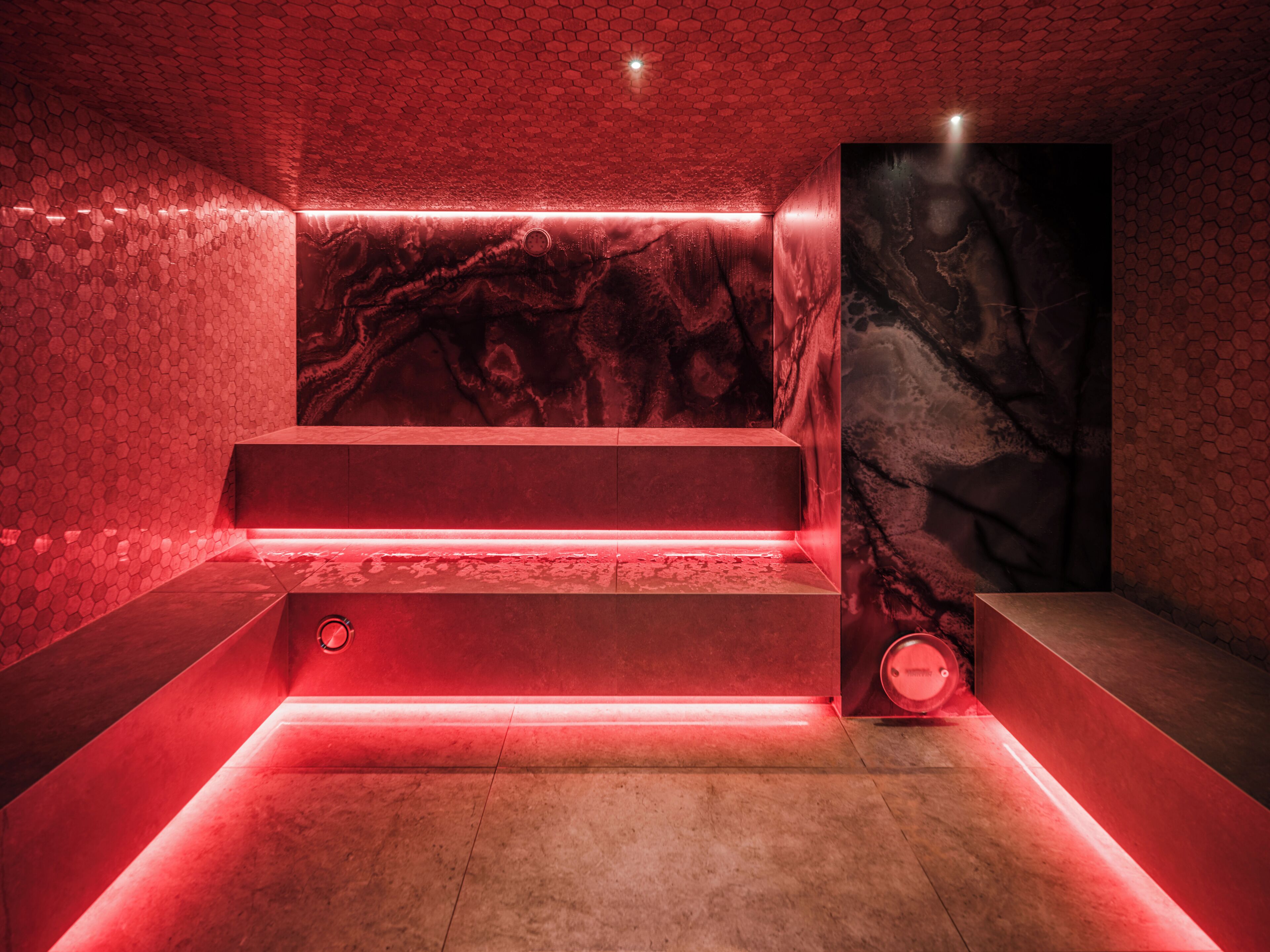 A modern interior with a red-lit reception desk, a marble wall, and a hexagonal patterned ceiling.